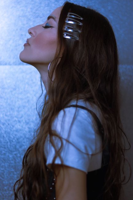 Profile portrait of a woman with long hair and hair clips against a textured blue background, showcasing her serene expression.
