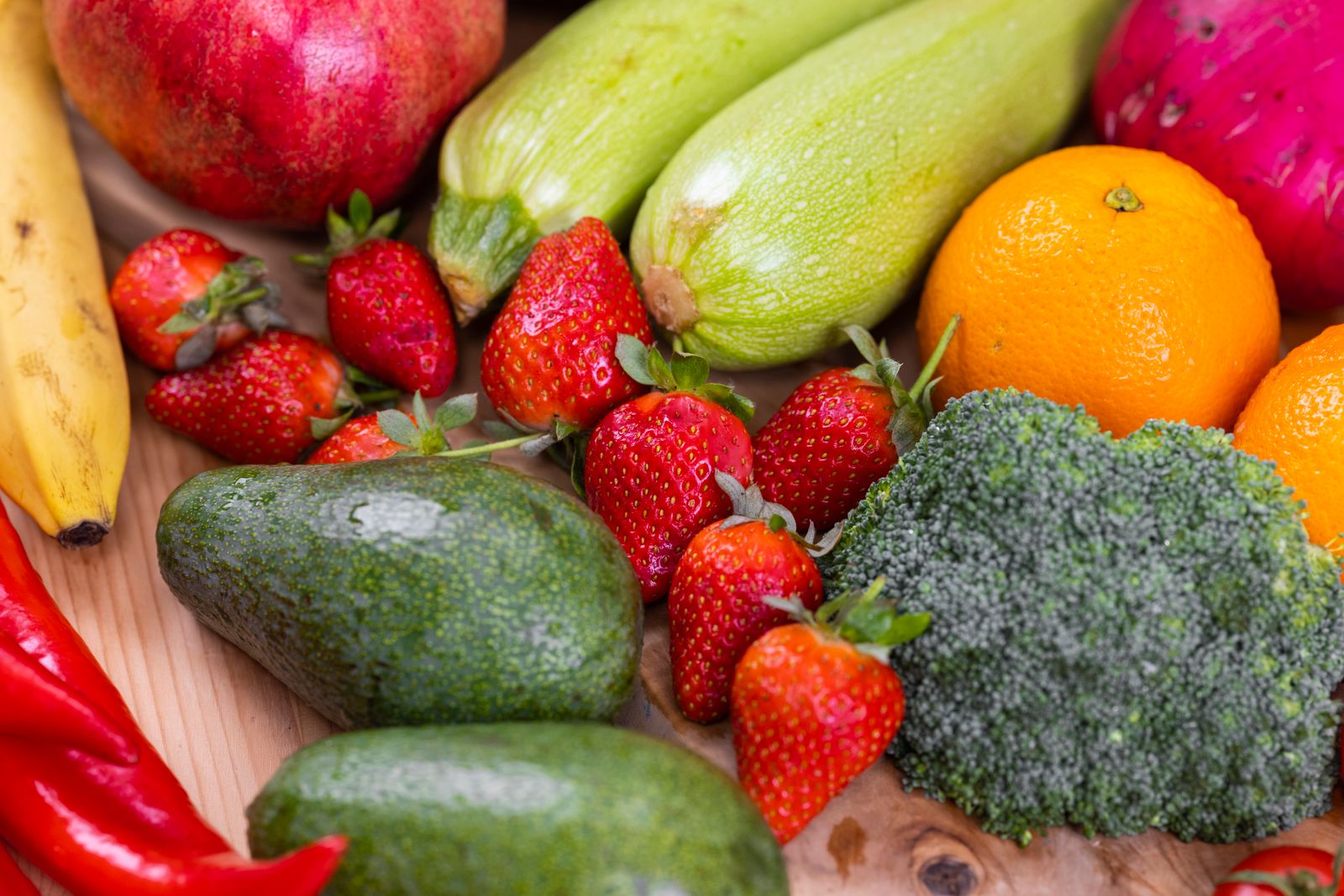 A vibrant selection of fresh strawberries, avocado, and broccoli on a wooden table, representing balanced sattvic foods for yoga