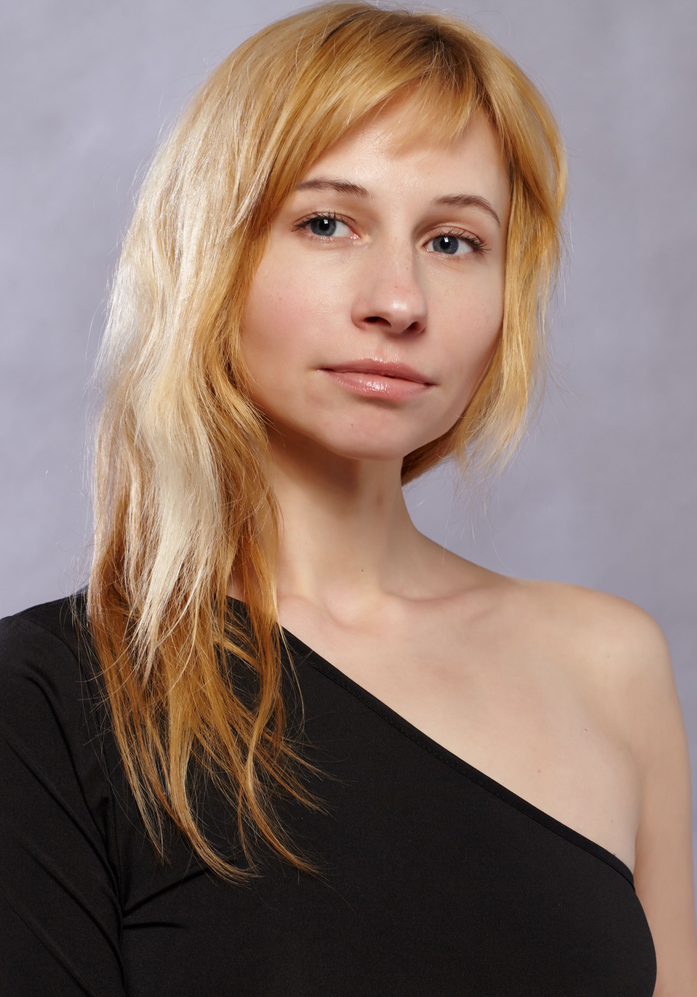 A beautiful woman with blonde hair poses elegantly in a one-shoulder top.