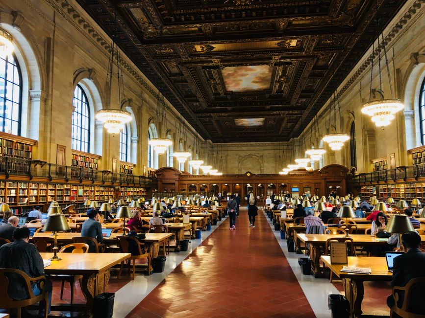 Busy reading room inside the New York Public Library featuring grand architecture.