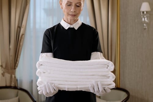 Free Woman in Black and White Uniform Holding a Stack of Towels Stock Photo