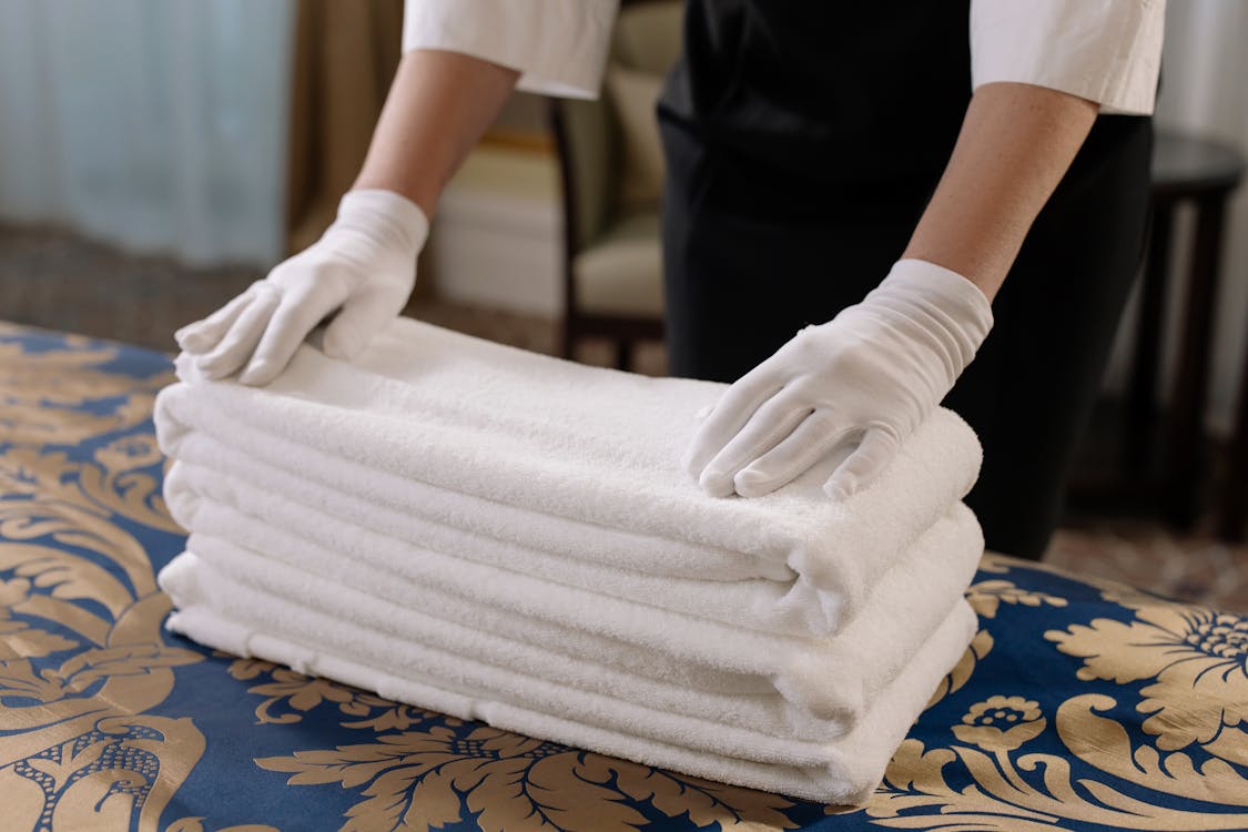 Free Professional housekeeper folding clean towels on a bed in a hotel room, emphasizing neatness and service. Stock Photo