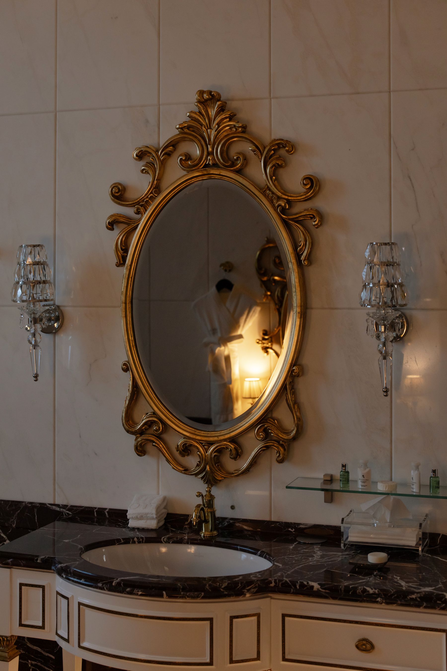 Classic bathroom sink with ornate oval mirror and paired wall lamps