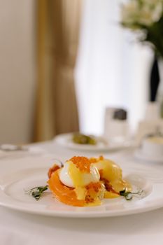 Gourmet breakfast featuring poached egg, salmon, and caviar on a plate, elegantly presented.