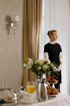 Elegantly dressed staff stands ready in a hotel room with a breakfast tray.