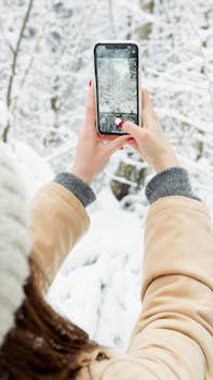 Woman taking a photo of a snowy landscape with a smartphone outdoors.