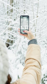 A person takes a photo of a snowy landscape using a smartphone in winter.