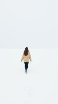 A person seen from behind walking across a vast, empty snowy field with a minimalist scene.