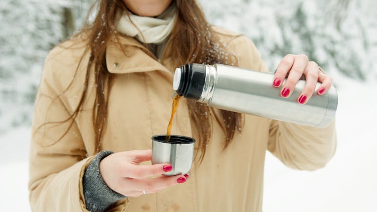 Woman In Brown Coat Pouring Coffee From A Tumbler