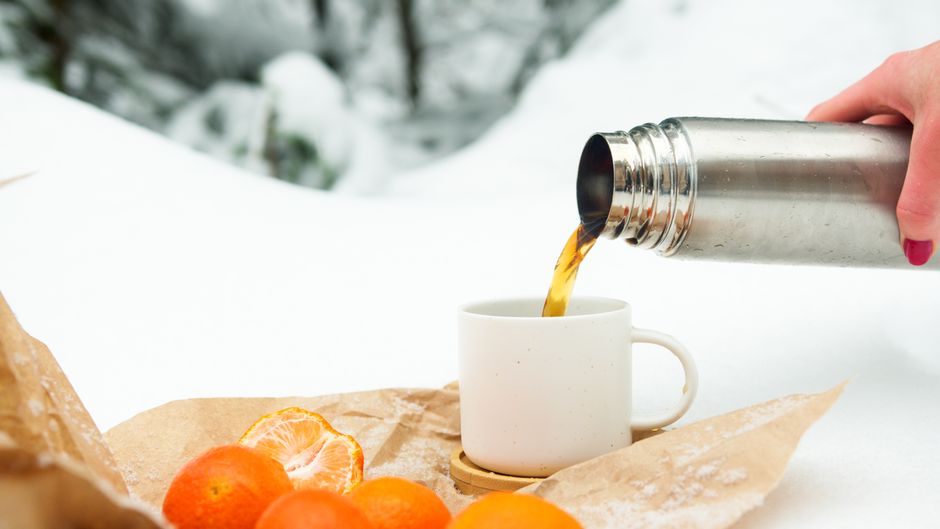 Pouring hot drink from thermos during a snowy winter picnic with oranges.