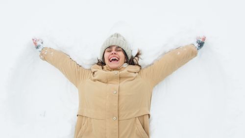 Free A woman enjoying winter fun, smiling while making snow angels outdoors. Stock Photo