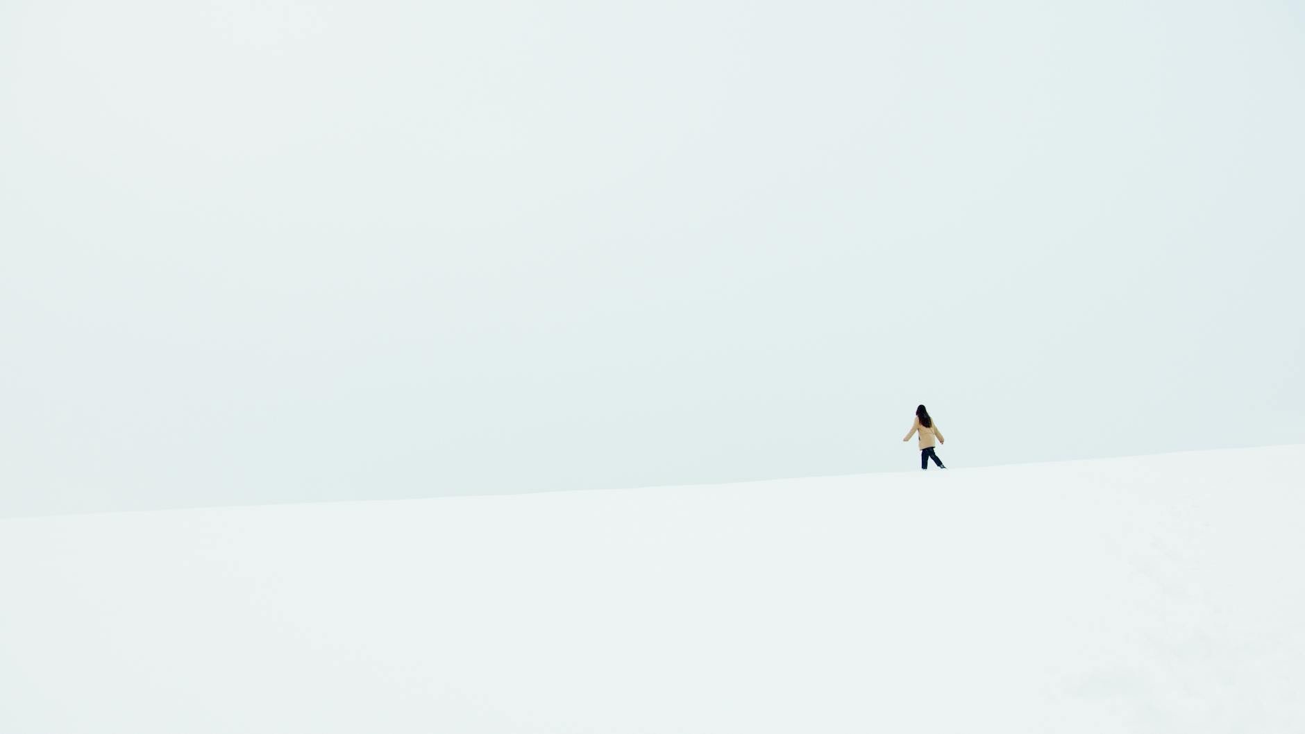 A woman walks alone in a vast, snowy landscape under a minimalistic, pale sky.