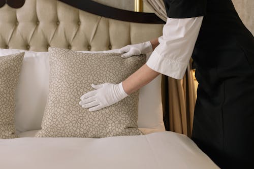 Woman with White Gloves Arranging a Pillow on Bed