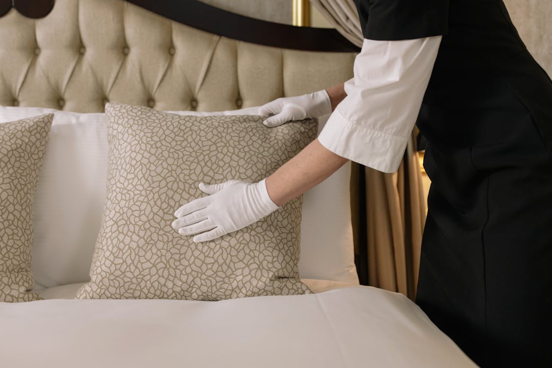 Free Woman with White Gloves Arranging a Pillow on Bed Stock Photo