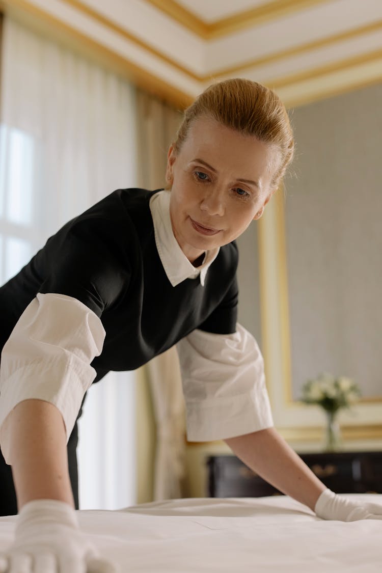 Woman Arranging Bed Linen In A Hotel Room