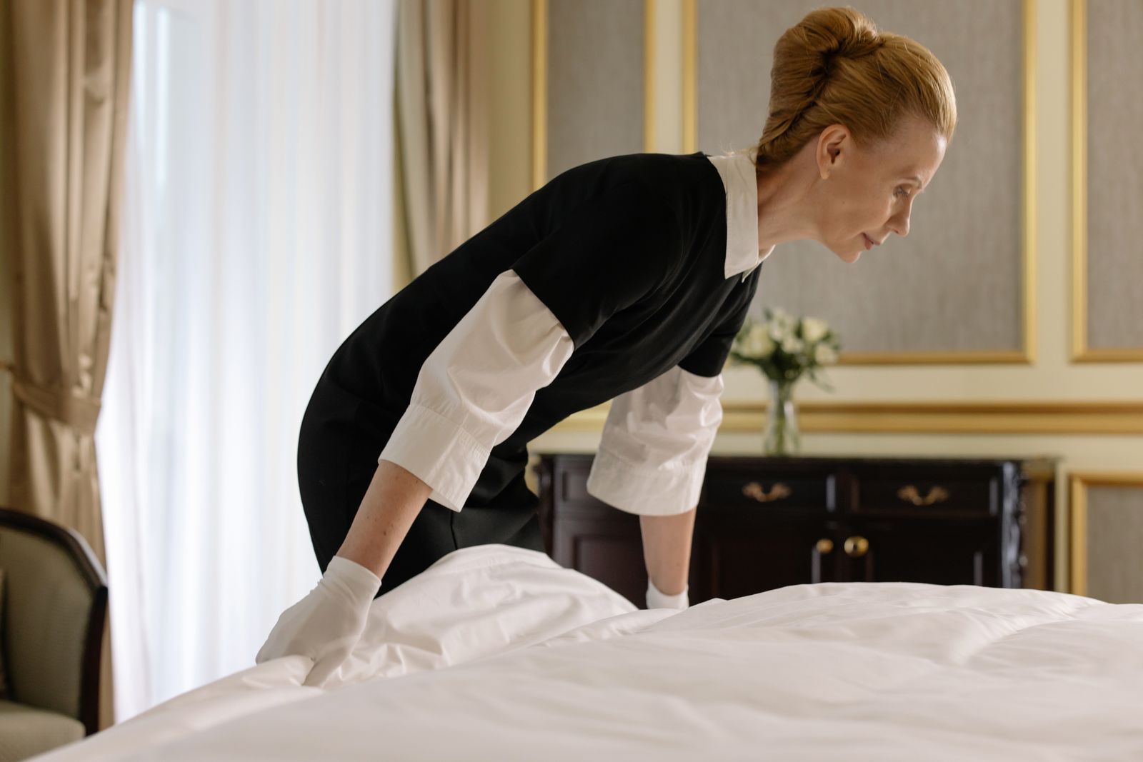 Rengøringsmedarbejder fra Tryg Hånd i mørk uniform, der retter sengetøj på et eksklusivt hotelværelse