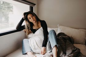 Woman in a black top and jeans relaxing on a bed beside a bright window