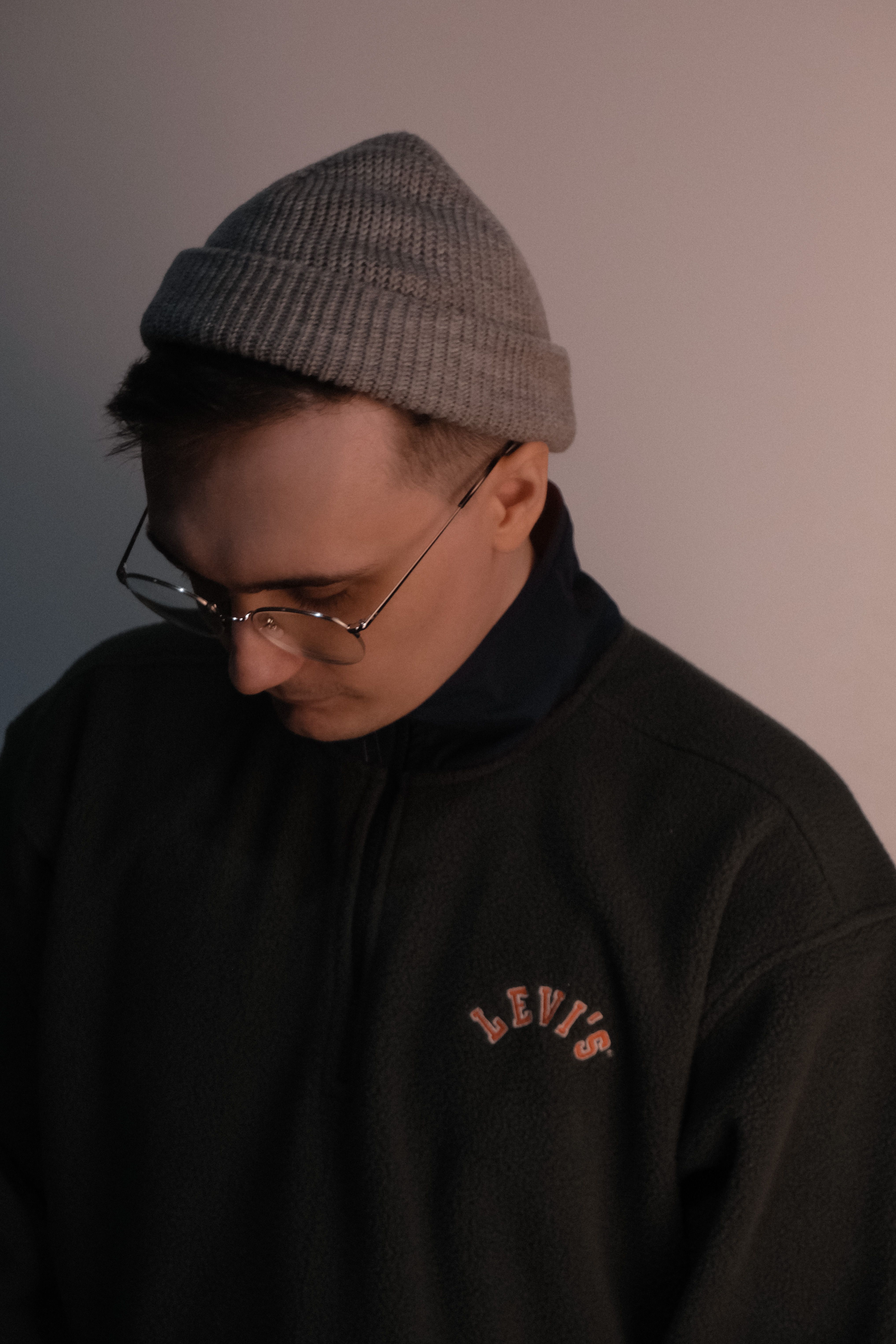 Side profile of a man in glasses and a beanie, wearing a sweatshirt, looking thoughtful.