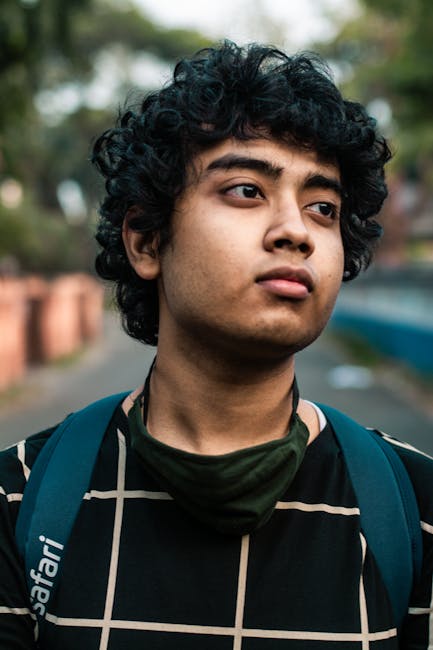 Portrait of a young man with curly hair, wearing a backpack and a checkered shirt outdoors.