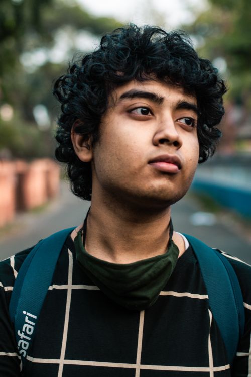 Free Portrait of a young man with curly hair, wearing a backpack and a checkered shirt outdoors. Stock Photo