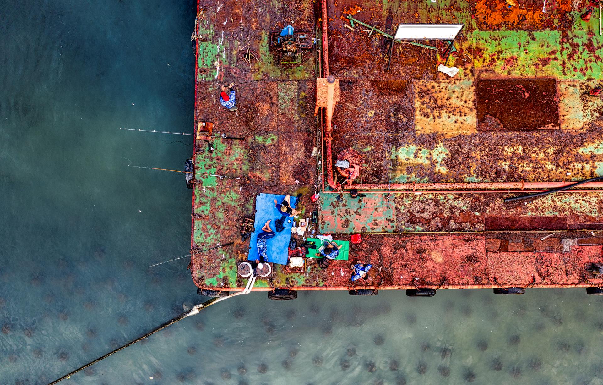 Aerial view of a rusty cargo ship with people onboard at Jakarta port, Indonesia.