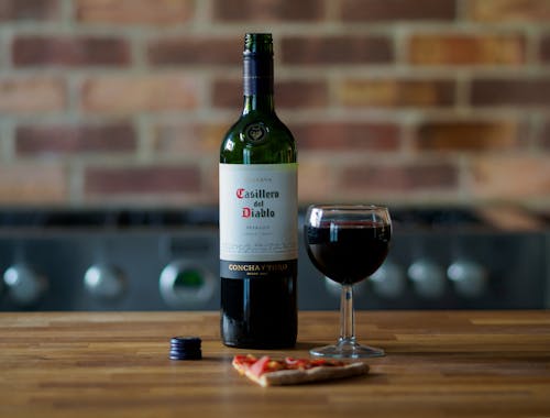 Glass of Wine and Bottle Beside a Pizza Slice on Wooden Surface
