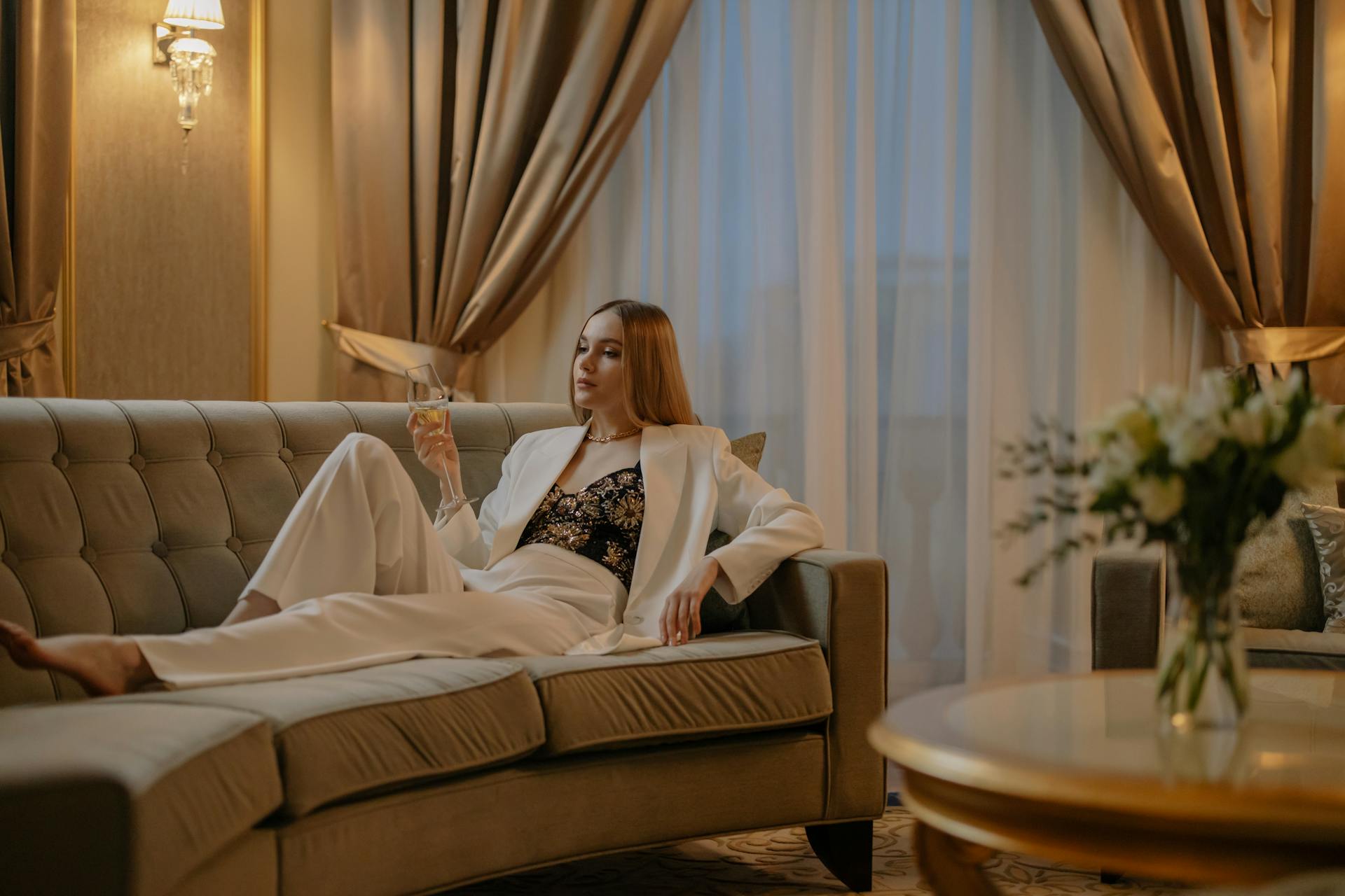 Woman in White Suit Sitting on Sofa with a Glass of Wine