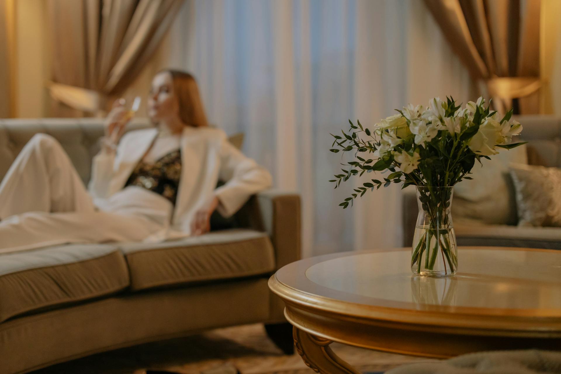 Luxurious hotel room with white flowers and a woman relaxing, creating a serene atmosphere.