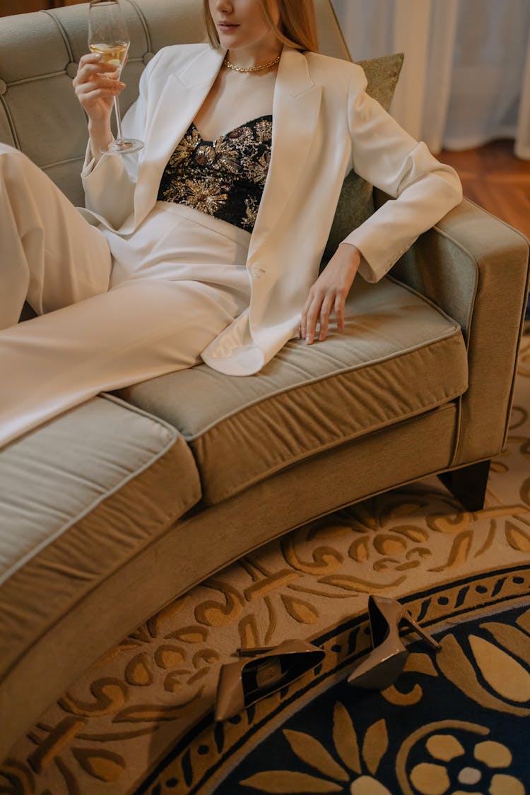 Woman In White Suit Sitting On Sofa Drinking Wine