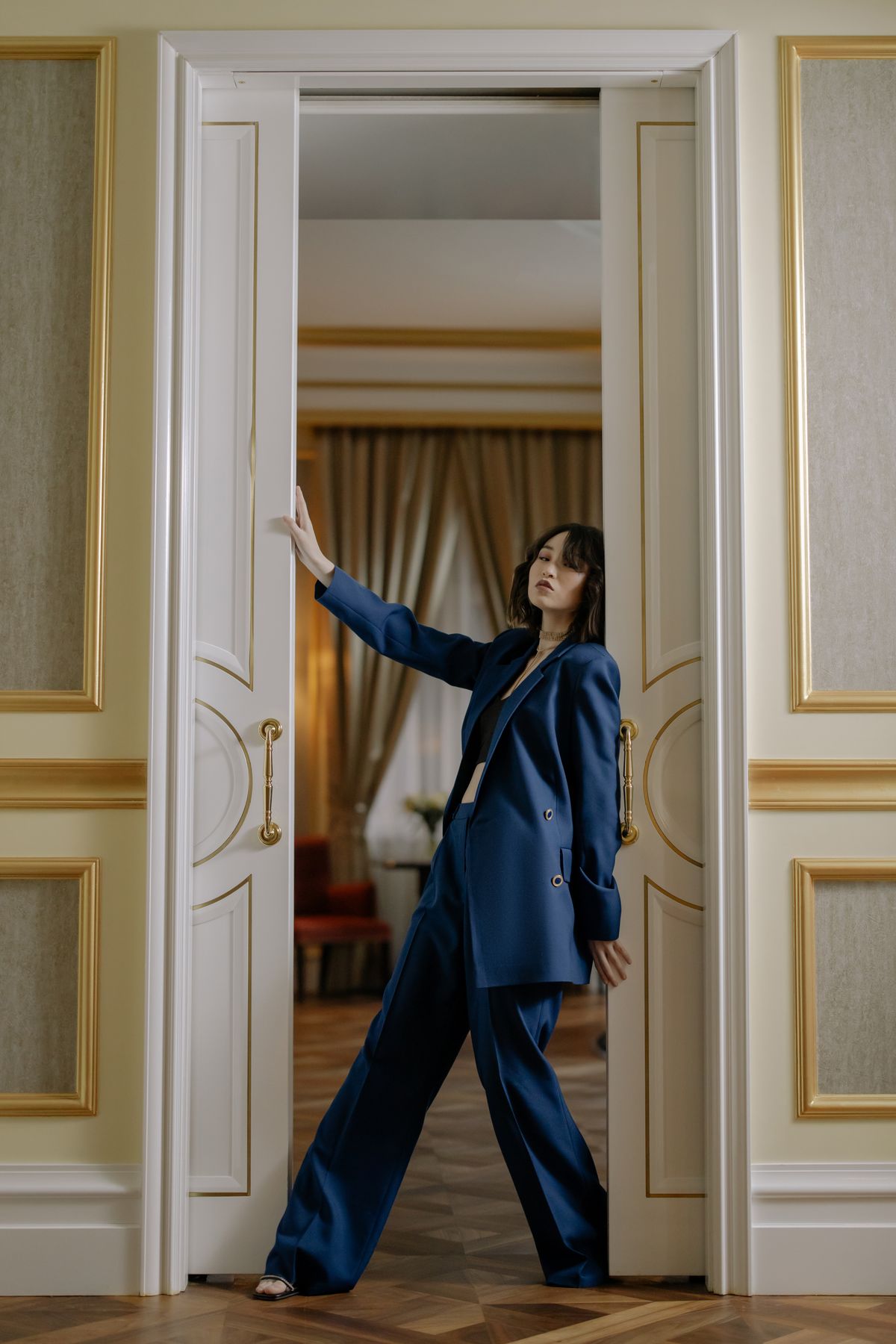 A woman in a tailored blue suit leaning against a door — relaxed summer tailoring