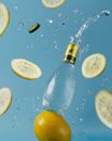 Creative composition of opened bottle with refreshing soft drink soaring on blue background near ripe lemon slices