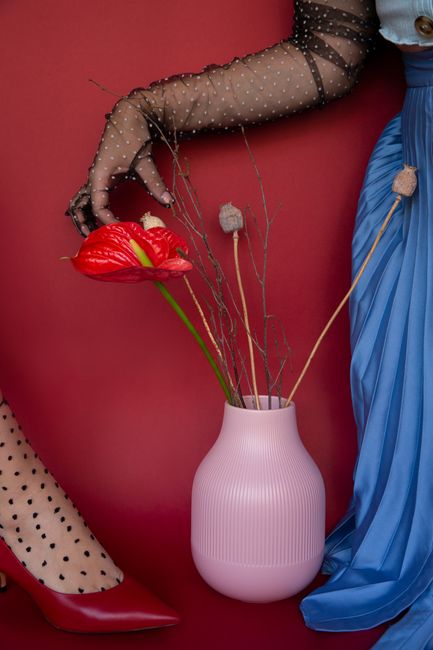 Crop anonymous female in elegant translucent lace gloves touching gentle red anthurium flower in vase in studio