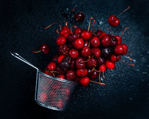 Top view composition of delicious sweet cherries and strainer scattered on dark background in studio