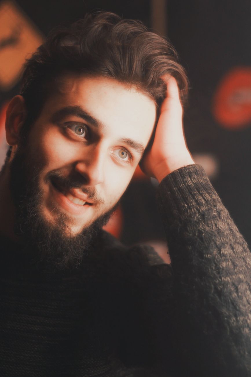 A warm and intimate portrait of a bearded man smiling and resting his head on his hand.