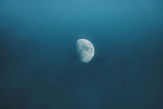 Waxing white moon with gray spots illuminating on foggy sky at bright night