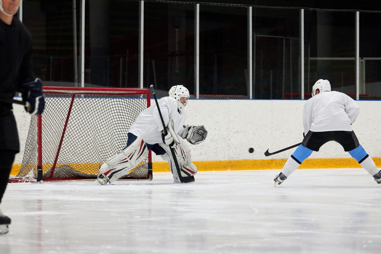 ice hockey action scene featuring a goalie in white gear defending aga