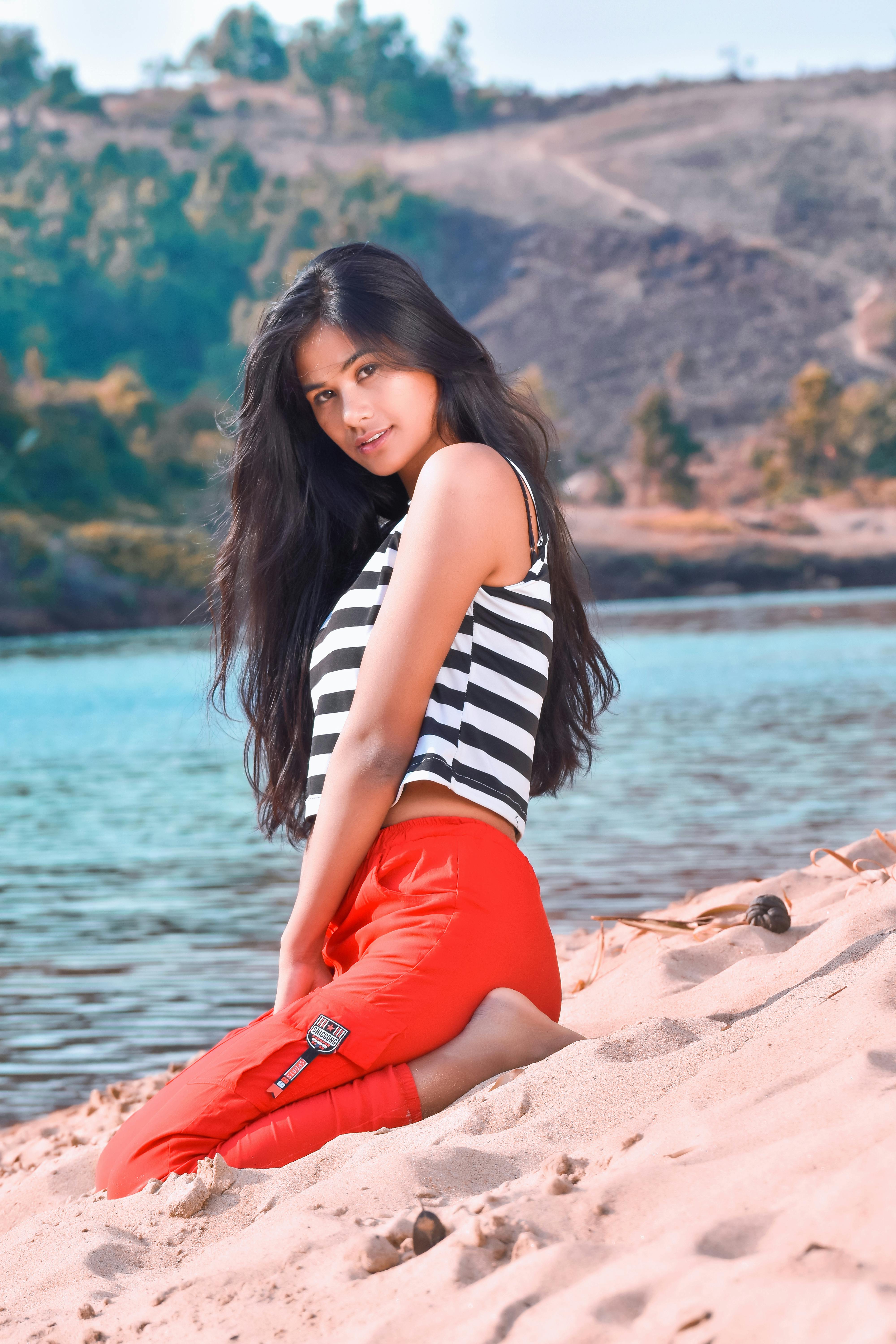 A young woman sits on sandy beach in striped top and red pants. Sunny day.