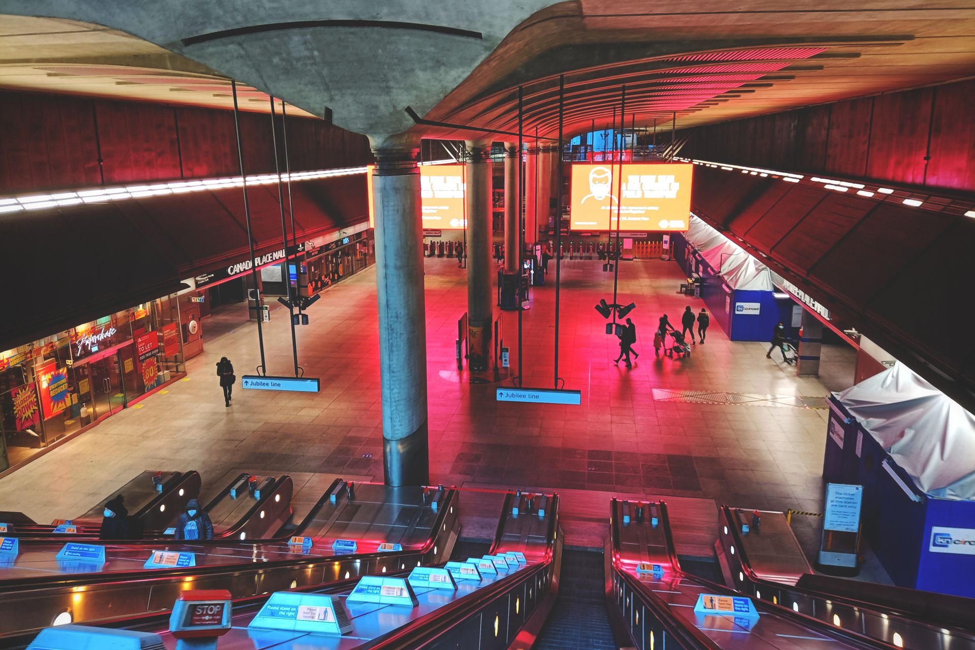 A vibrant urban subway station with escalators and commuters, featuring colorful lighting and advertisements.