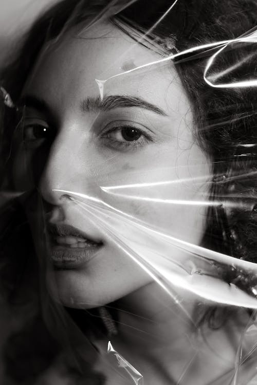 Black and white of young confident woman with cellophane wrap on face while looking at camera