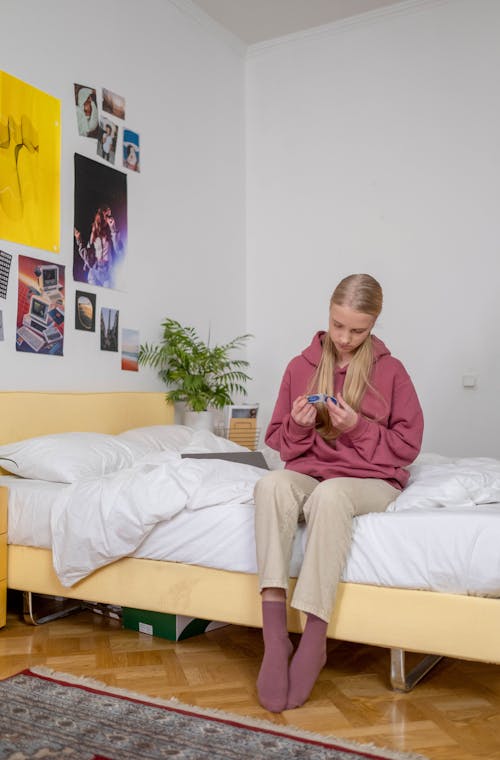 Free A Young Woman Looking at a pack of Condoms While Sitting on a Bed Stock Photo