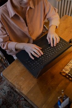 A woman typing on a laptop at a wooden table inside a cozy room, focusing on remote work.