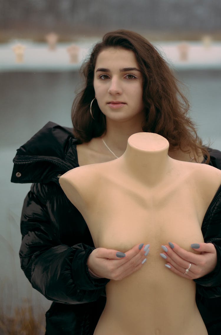 A Pretty Woman Posing While Holding A Mannequin's Breasts