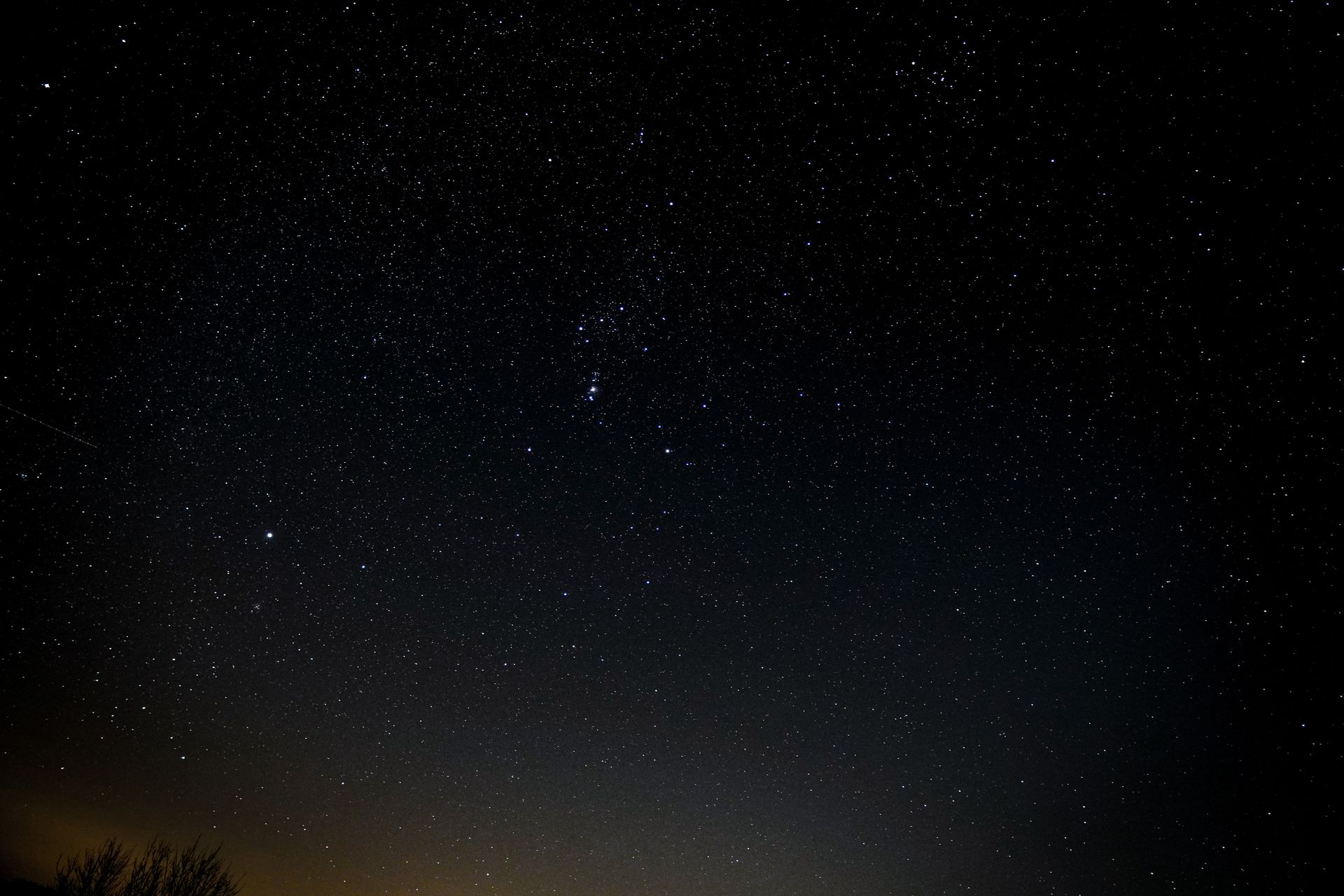 A stunning view of the starry night sky featuring the Orion constellation above a dark landscape.