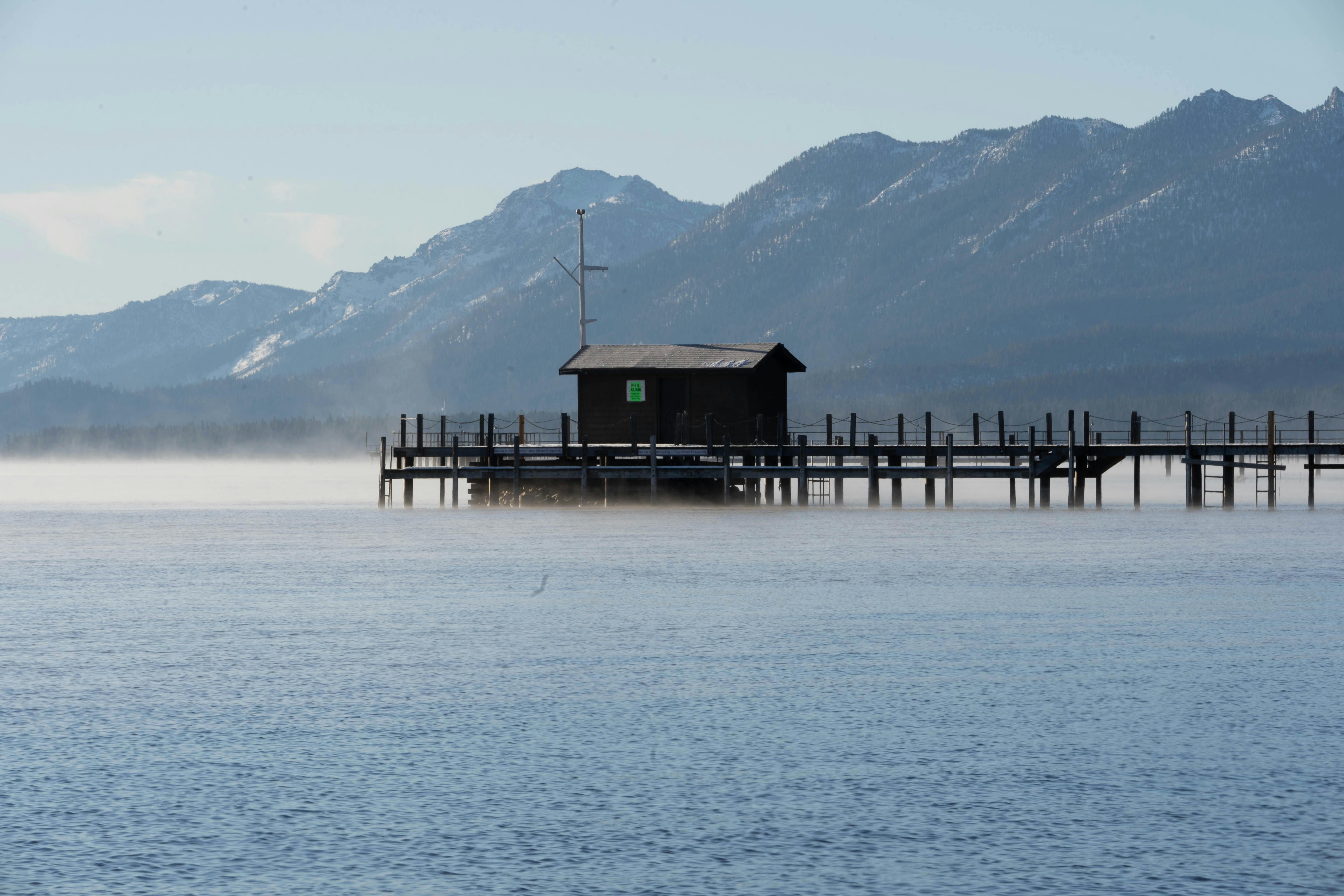 A tranquil scene of a wooden house on a pier with misty mountains in the background.