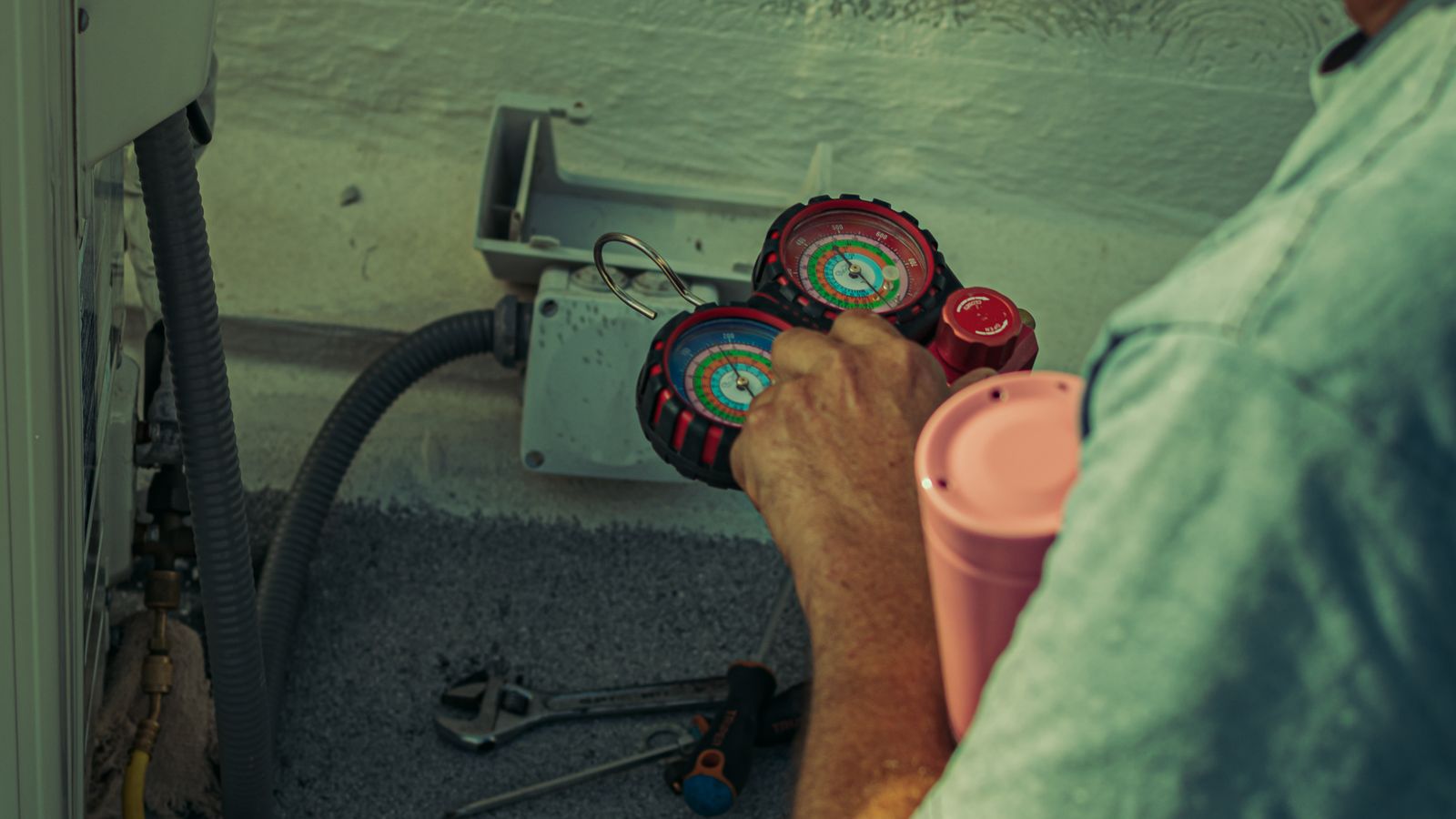 A technician reads the manifold gauges while servicing an outdoor air conditioning unit