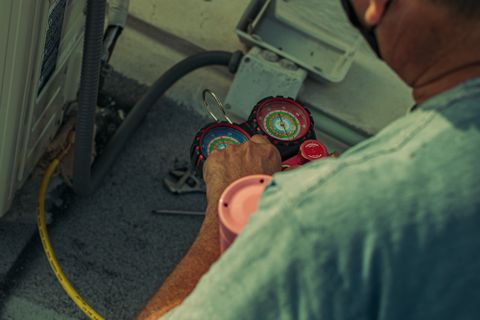 Technician working on an outdoor unit with gauges and tools