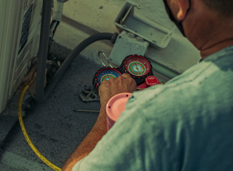 Technician working on an outdoor unit with gauges and tools