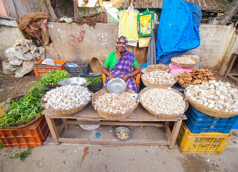 Colorful street market scene of a senior vendor selling vegetables in Cumbum, India.