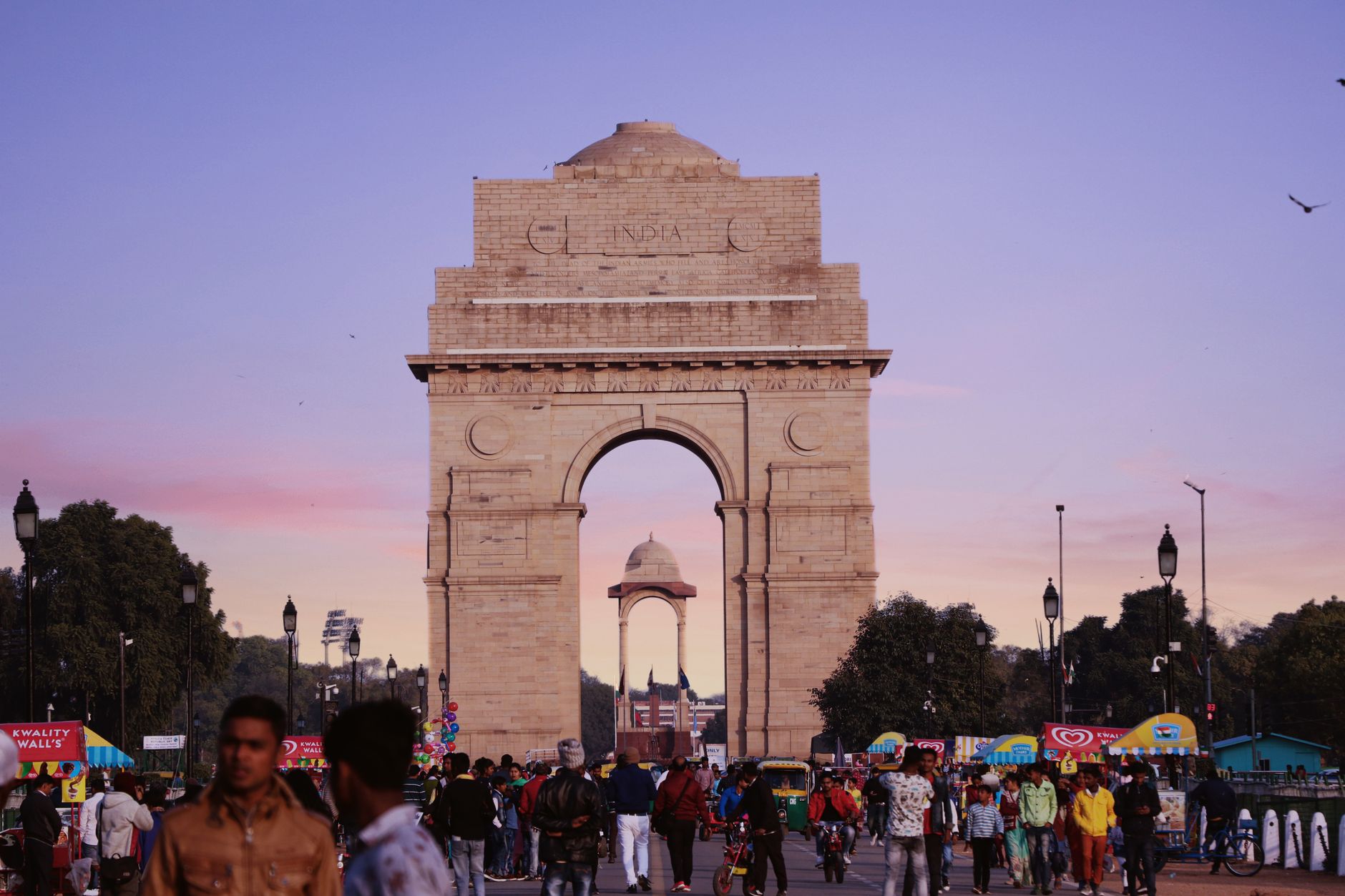 नई दिल्ली का इंडिया गेट सुबह की सुनहरी रोशनी में, सामने शांत सड़क और राष्ट्रीय ध्वज