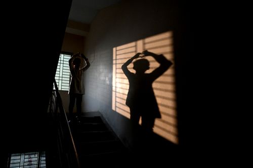 Free A person creates a silhouette on a stairway with dramatic shadows from a window. Stock Photo